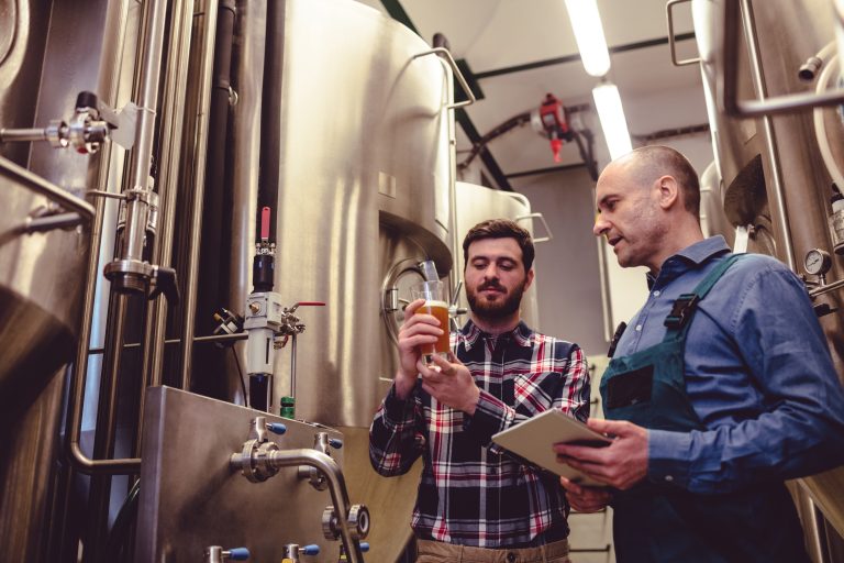 dos hombres inspeccionan el proceso de elaboración de cerveza en una cervecería